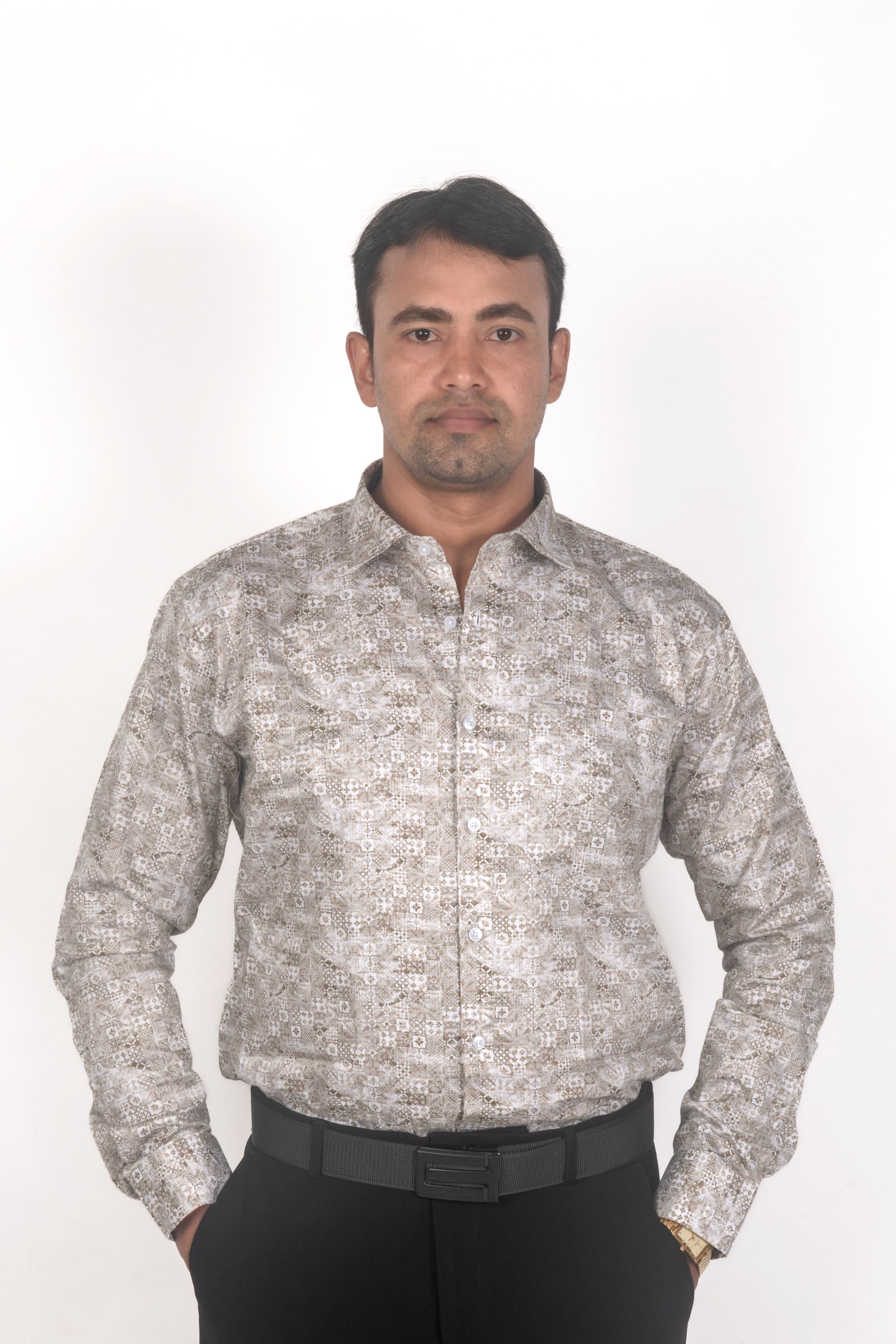 A man wearing a long-sleeve button-up shirt with a beige and white abstract pattern, paired with black trousers and a black belt, standing against a plain white background.
