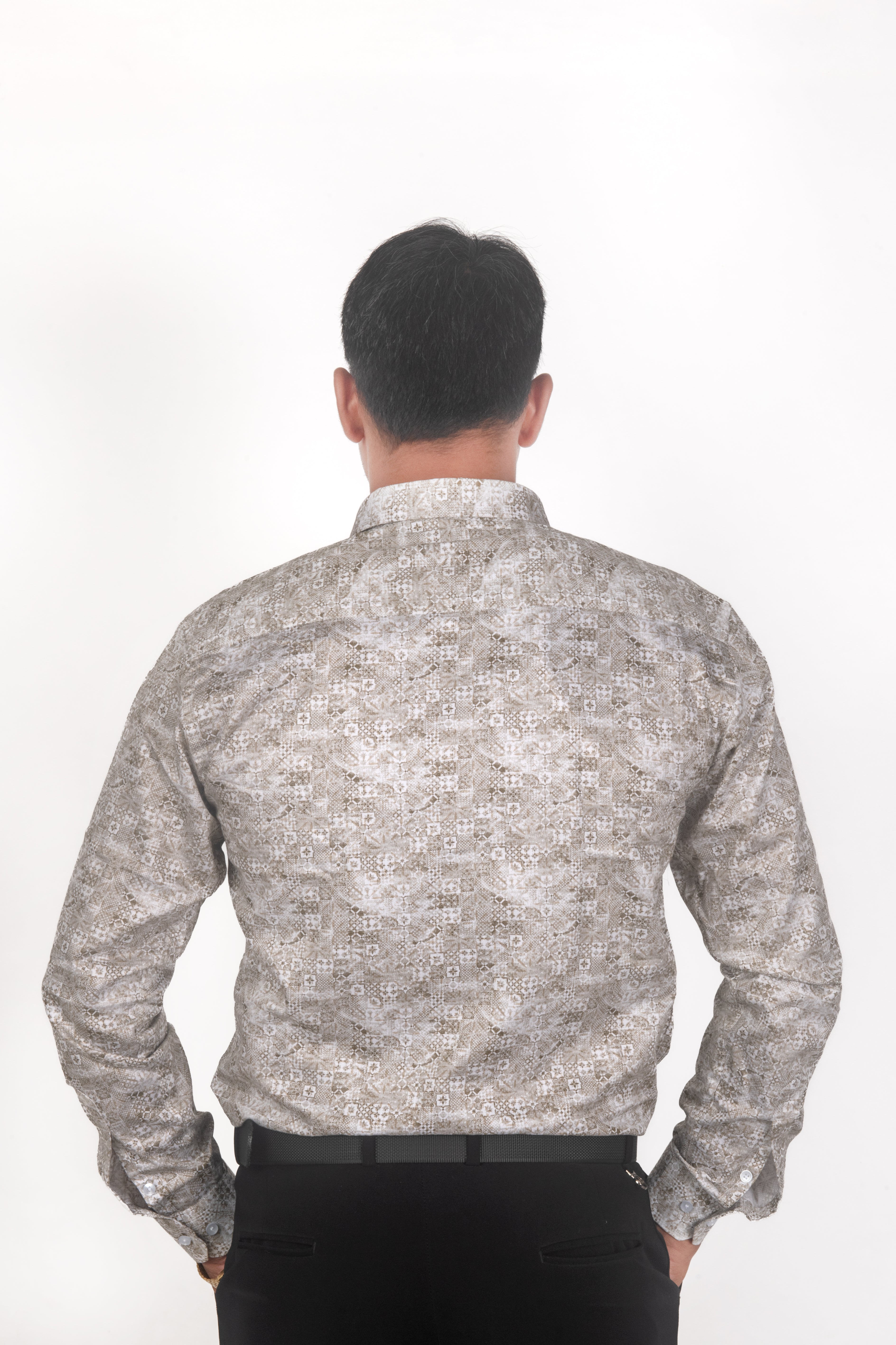A man viewed from behind wearing a long-sleeve button-up shirt with a light beige and gray geometric pattern, paired with black trousers, against a plain white background.