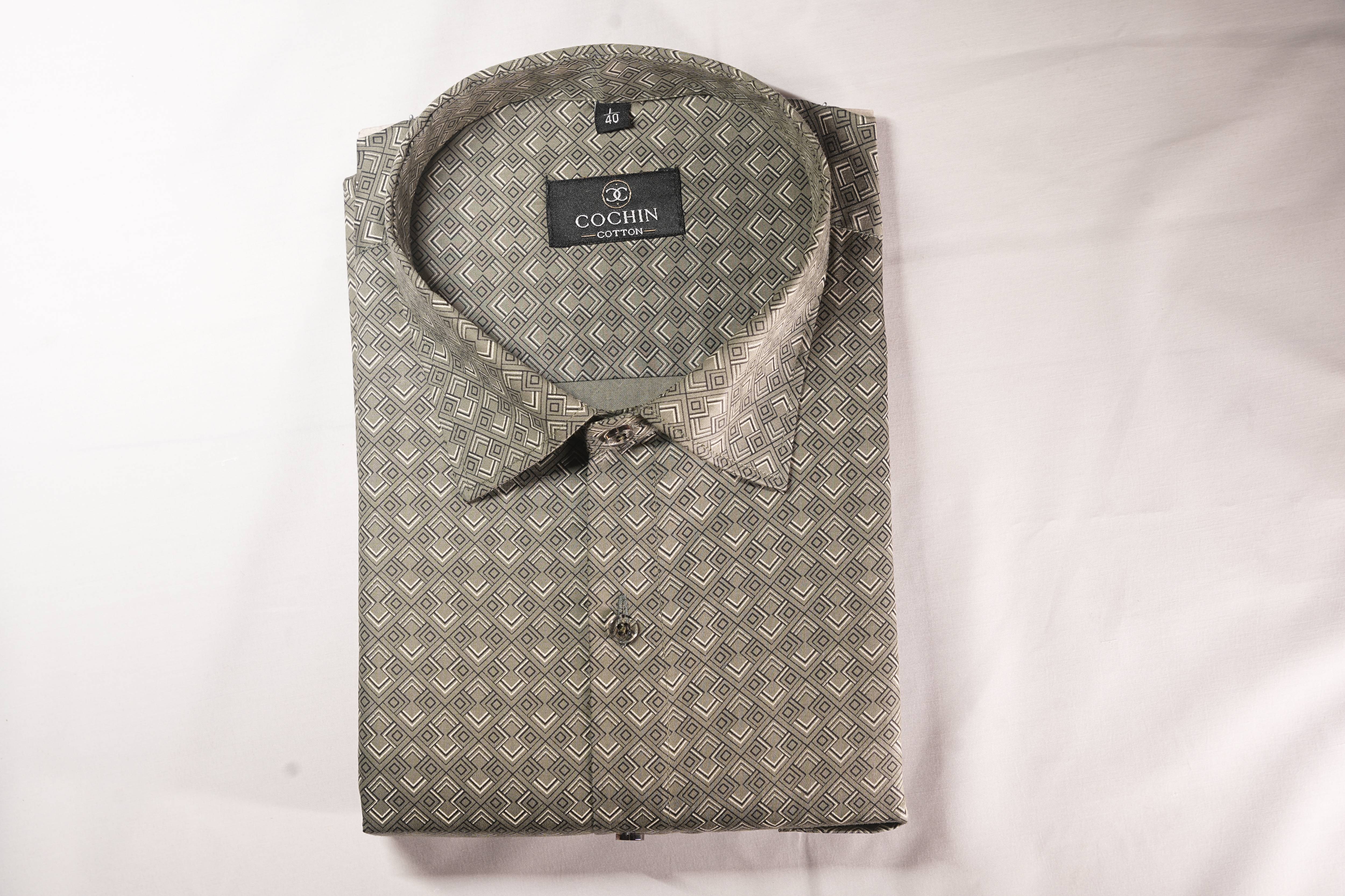 A folded men's dress shirt with a geometric pattern in olive green and beige, featuring a pointed collar and a visible Coachin brand label.