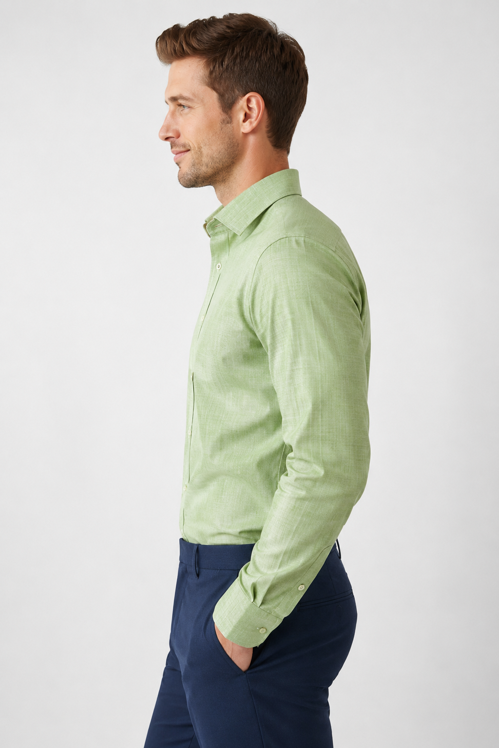 Man wearing a light green dress shirt and dark blue pants on a white background