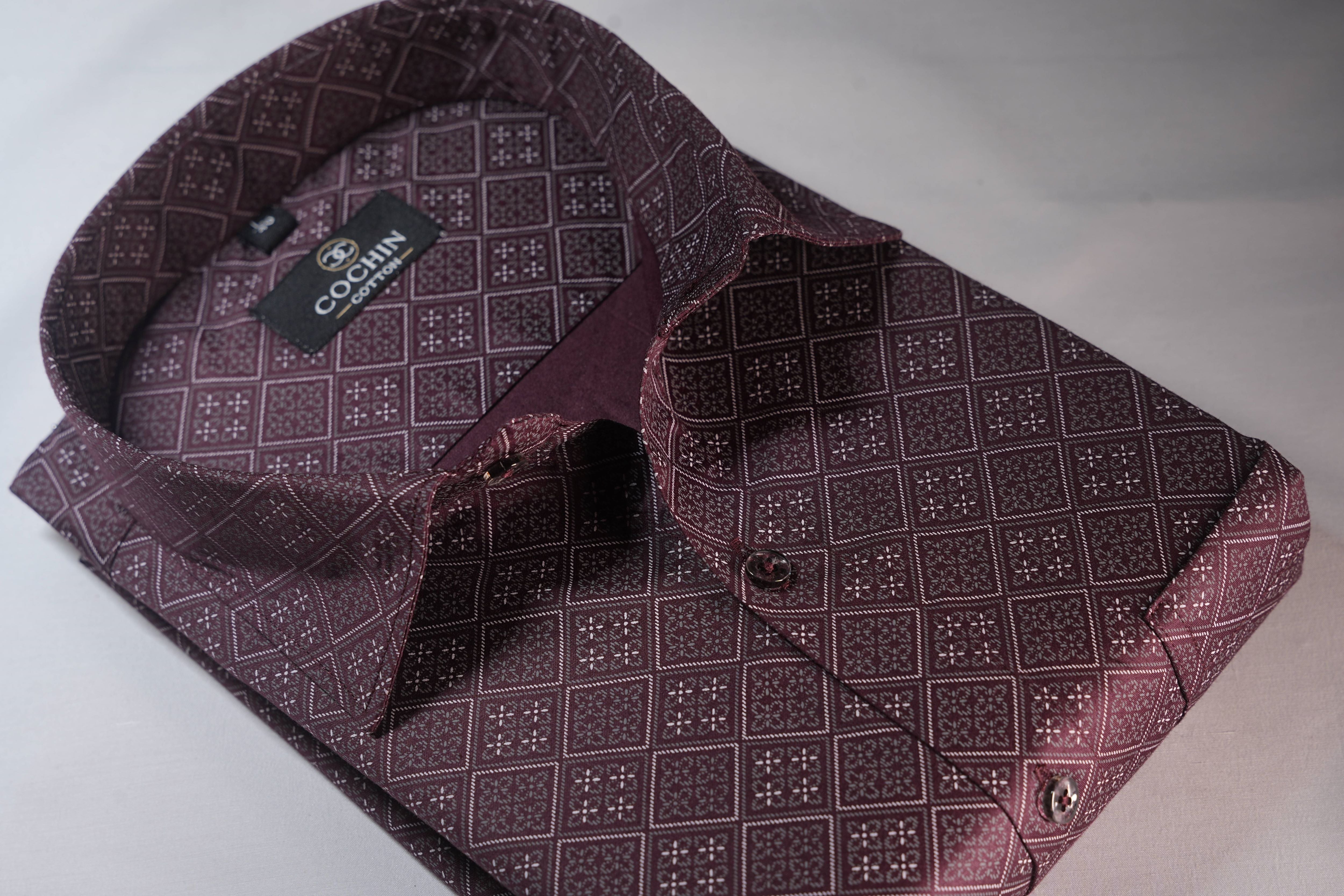 Folded maroon patterned shirt with a brand label on a light gray background