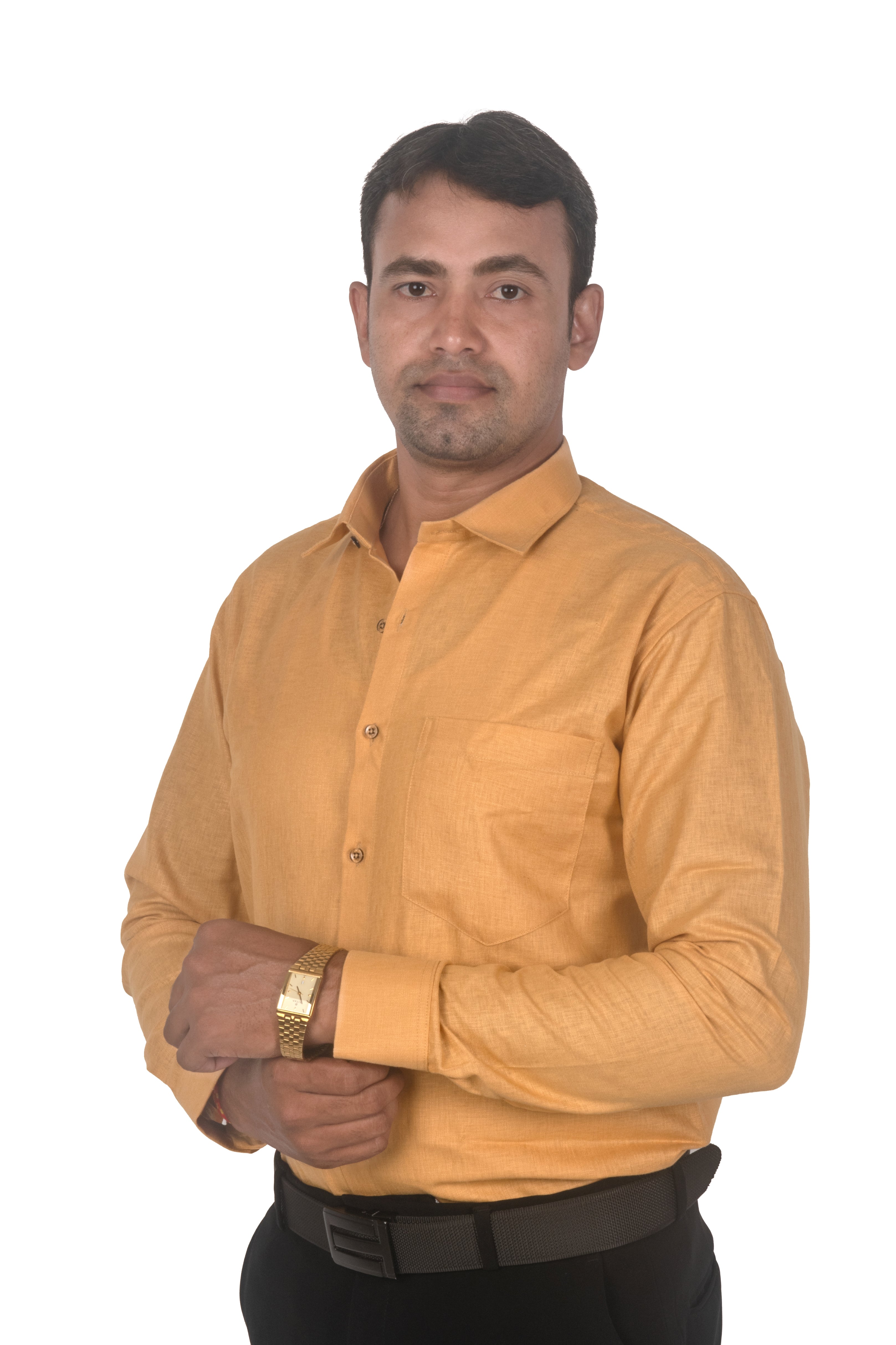 A man wearing a mustard yellow long-sleeve button-down shirt, black trousers, and a gold watch, standing against a plain white background.