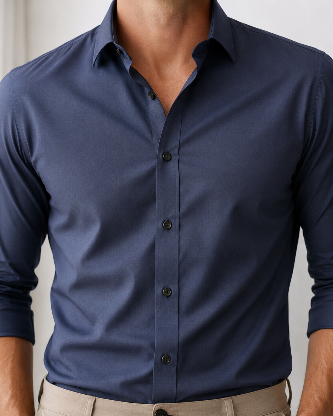A man wearing a navy blue long-sleeve button-down dress shirt tucked into beige trousers, shown from the neck down in a clean studio setting.