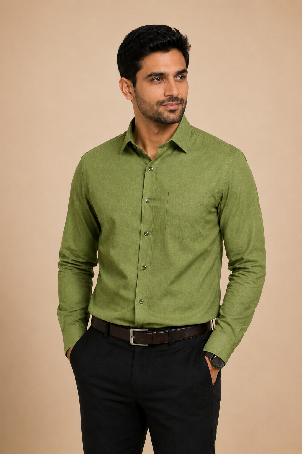 A man wearing a long-sleeve olive green button-down shirt, black trousers, and a brown belt, standing against a solid beige background.