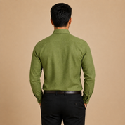 A man viewed from behind wearing an olive green long-sleeve linen shirt and black trousers, standing against a solid beige background.