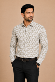 A man wearing a long-sleeve button-up shirt with a beige and white geometric pattern, paired with black trousers and a dark belt, standing against a solid beige background.