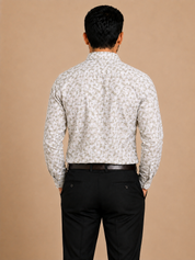 A man viewed from behind wearing a long-sleeve button-up shirt with a small beige and white floral pattern, paired with black trousers and a dark brown belt, against a solid beige background.