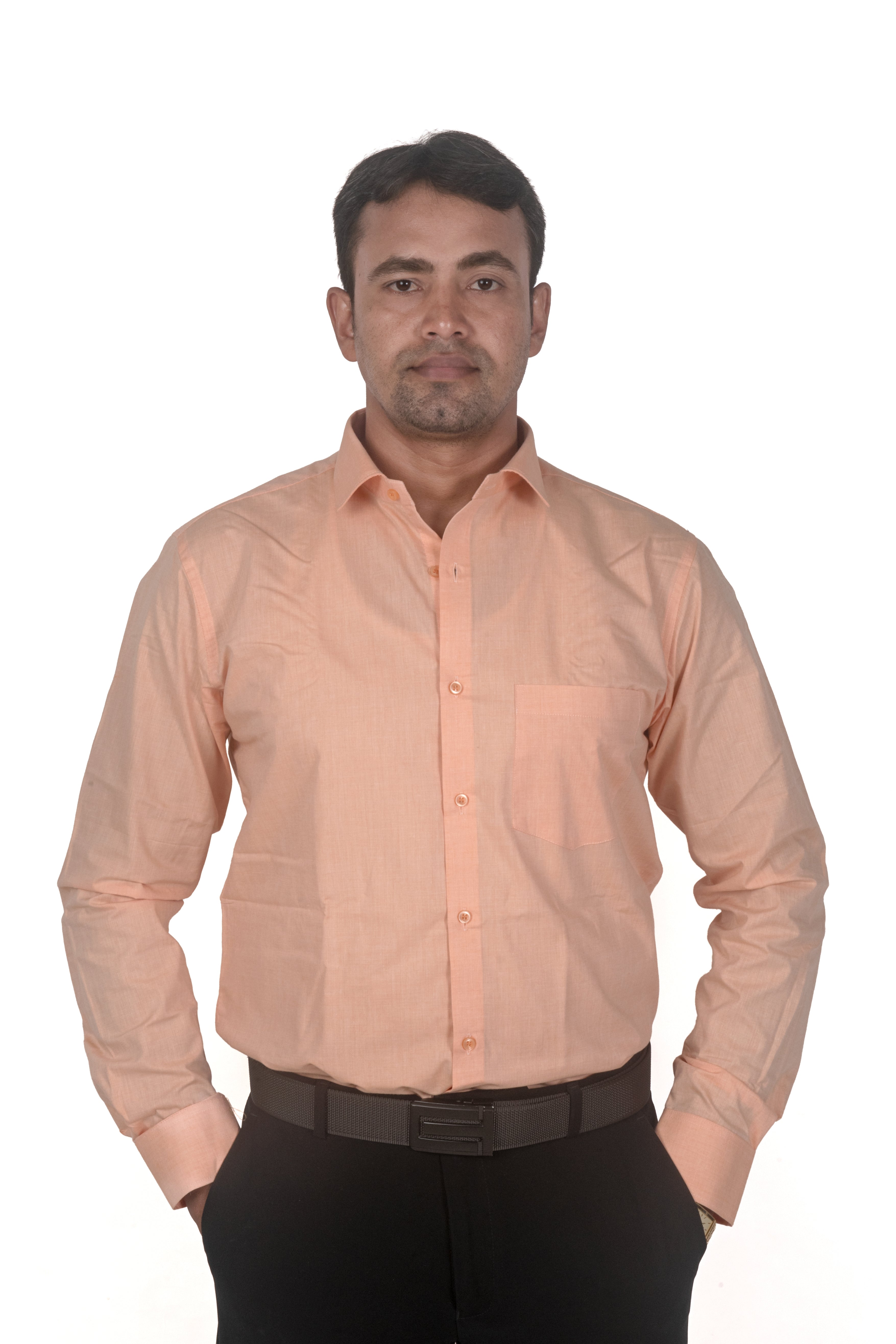 A man wearing a light peach-colored long-sleeve button-down shirt and black trousers, standing against a plain white background.