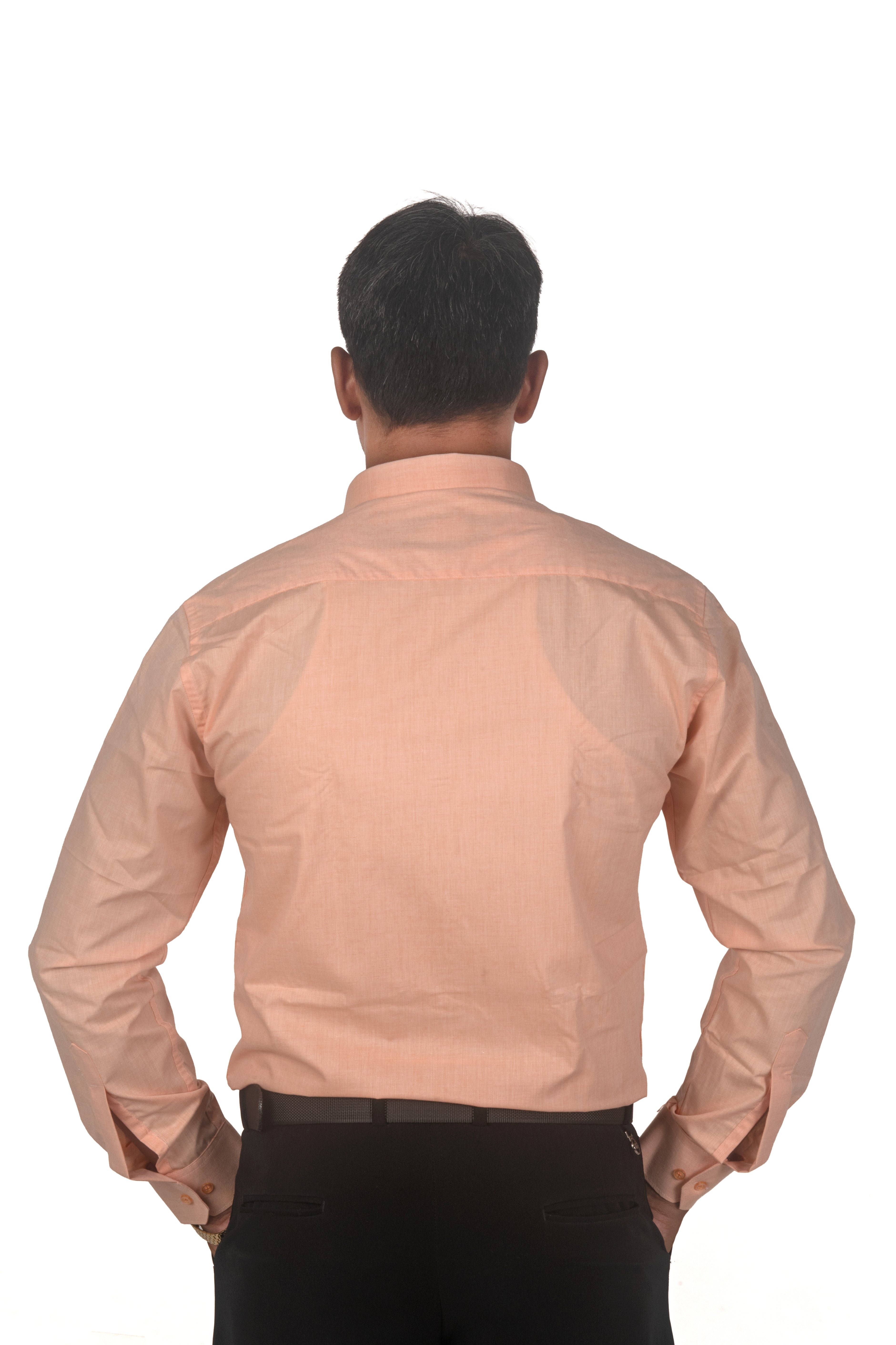 A man viewed from behind wearing a light peach-colored long-sleeve button-down shirt and black trousers, standing against a solid white background.