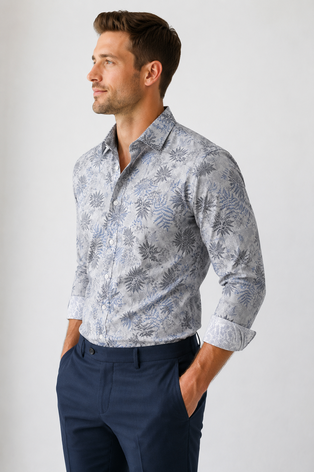 Man wearing a patterned shirt and navy pants against a plain background