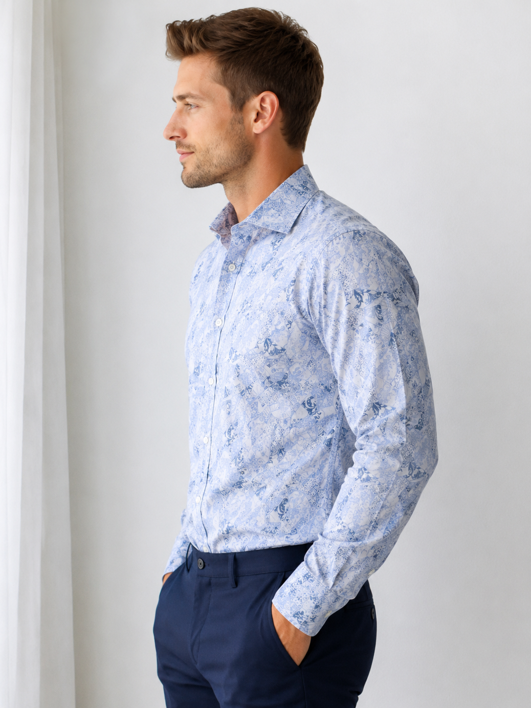 Man wearing a light blue floral shirt and dark blue pants against a white background