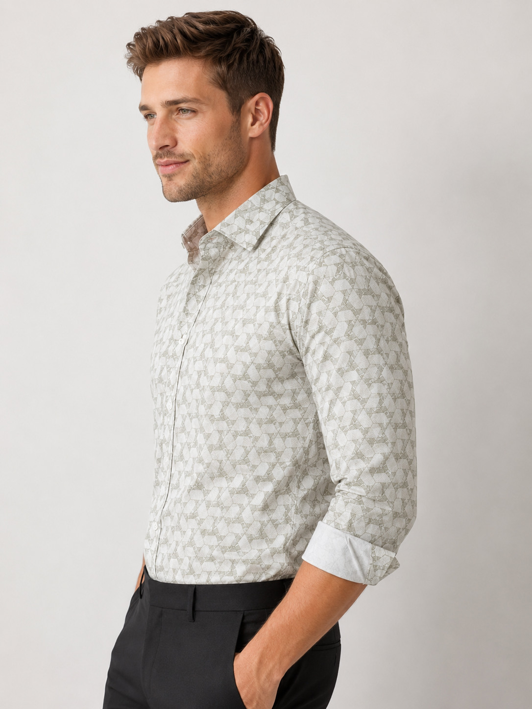 Man wearing a light gray patterned shirt with rolled-up sleeves against a plain background