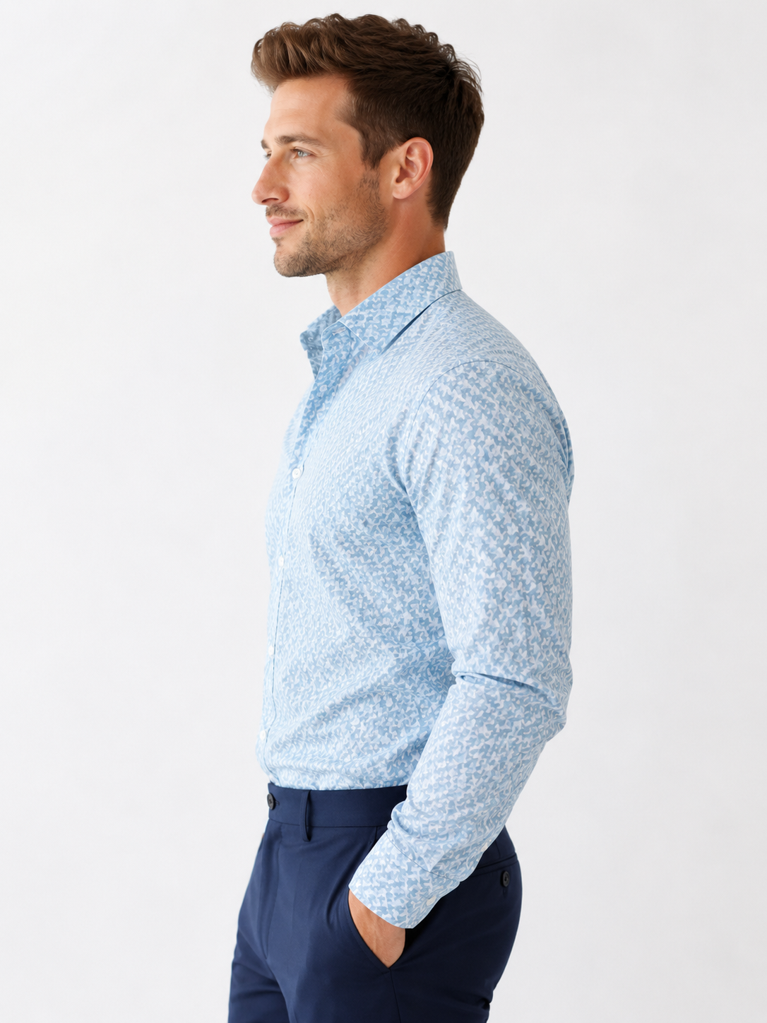 Man wearing a light blue patterned shirt and dark blue pants on a white background