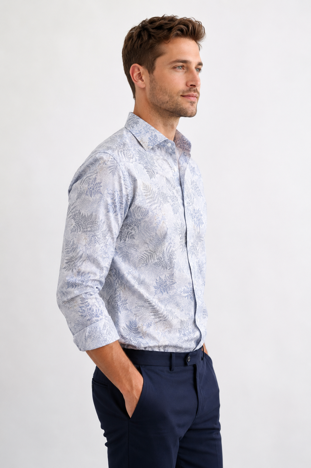 Man wearing a light blue patterned shirt and dark pants on a white background