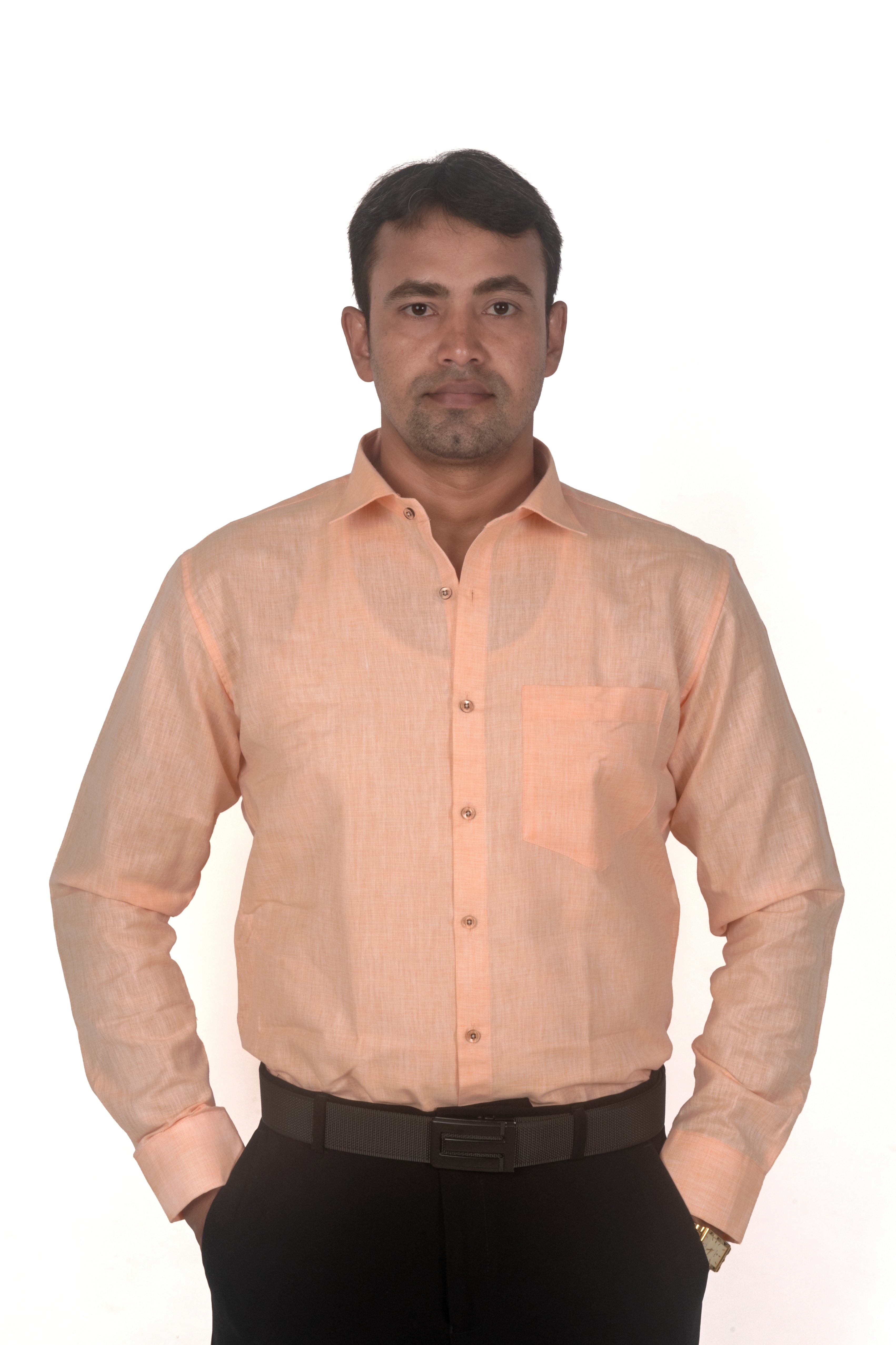 A man wearing a light peach-colored long-sleeve linen shirt with a chest pocket, paired with black trousers and a black belt, standing against a plain white background.