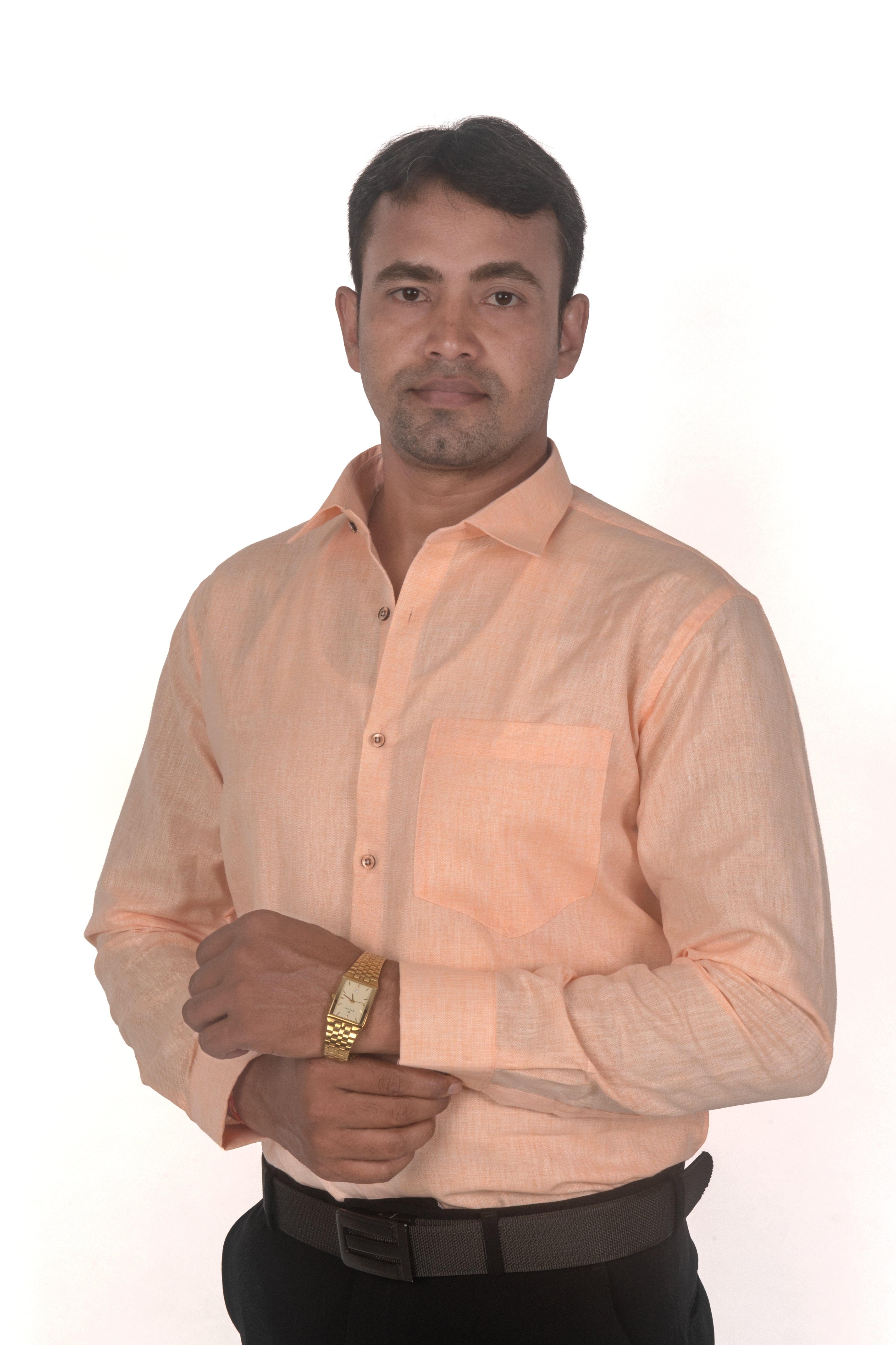 A man wearing a light peach-colored long-sleeve button-down shirt, black trousers, and a gold watch, standing against a plain white background.