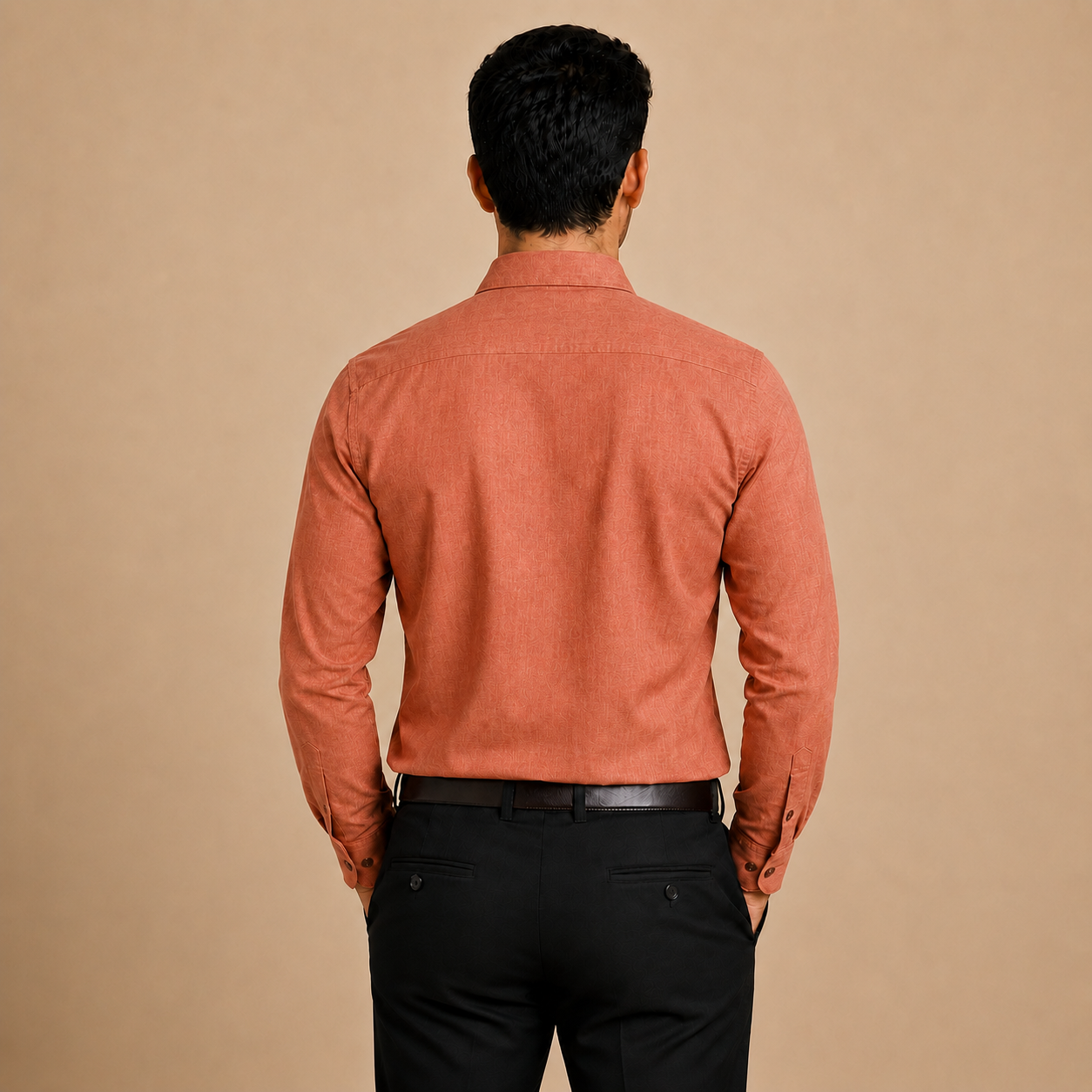 A man viewed from behind wearing a textured, muted orange-brown long-sleeve button-down shirt and black trousers, standing against a solid beige background.