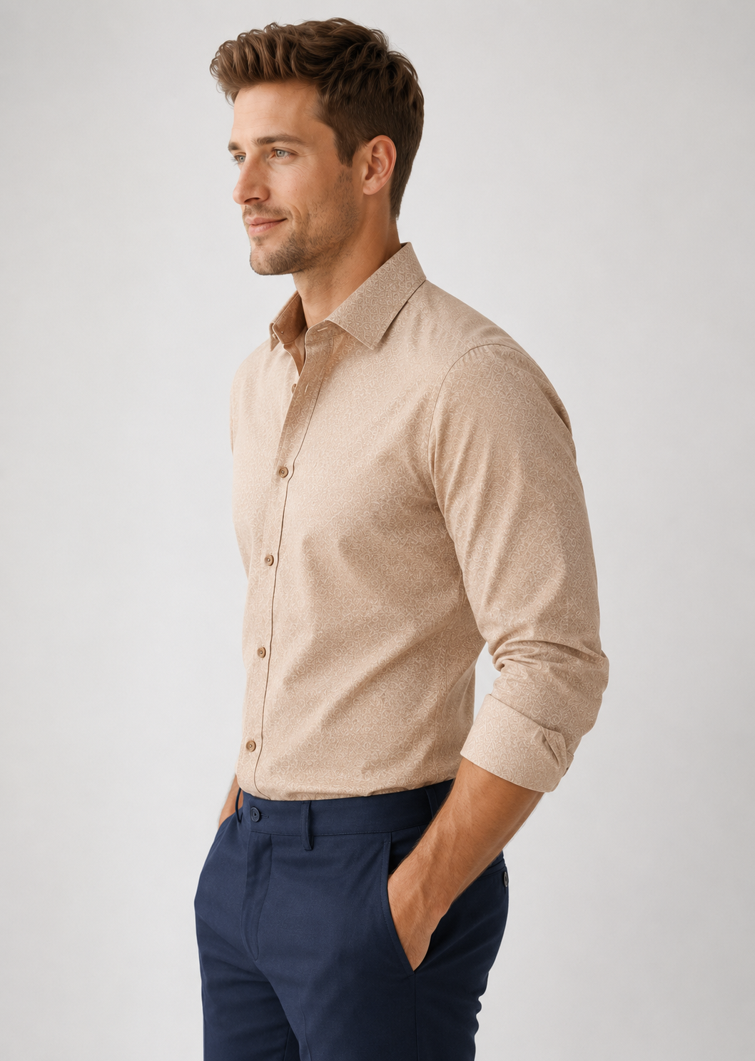 Man wearing a beige sweater over a brown shirt with navy pants on a light gray background
