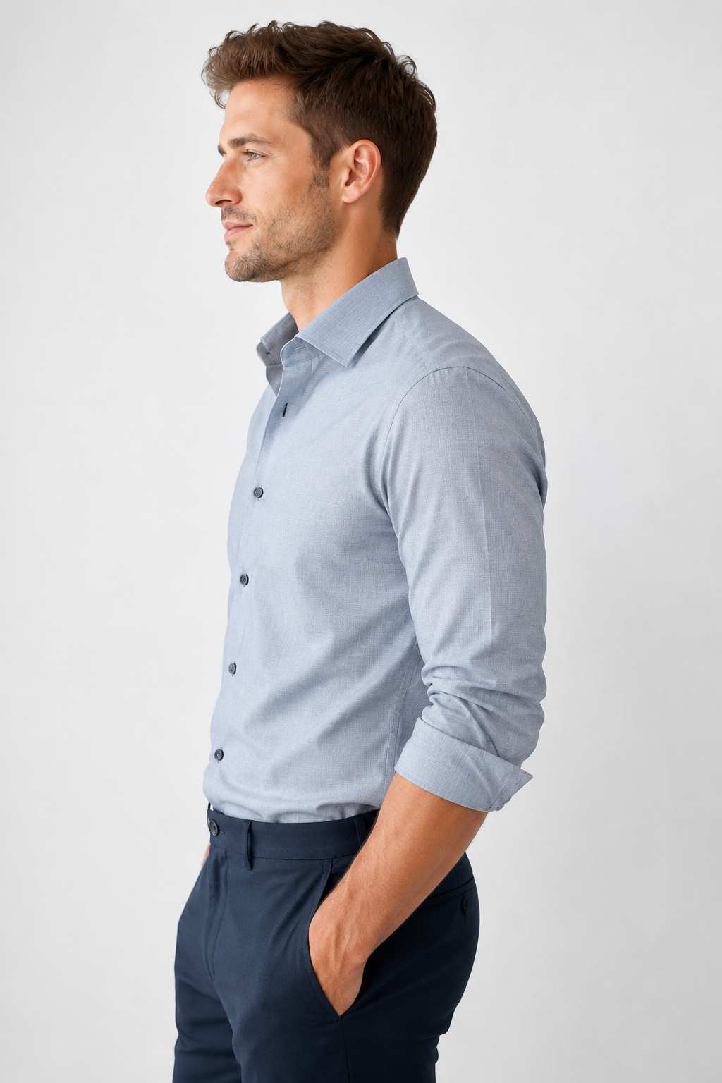 Man wearing a light blue button-up shirt and dark pants on a white background
