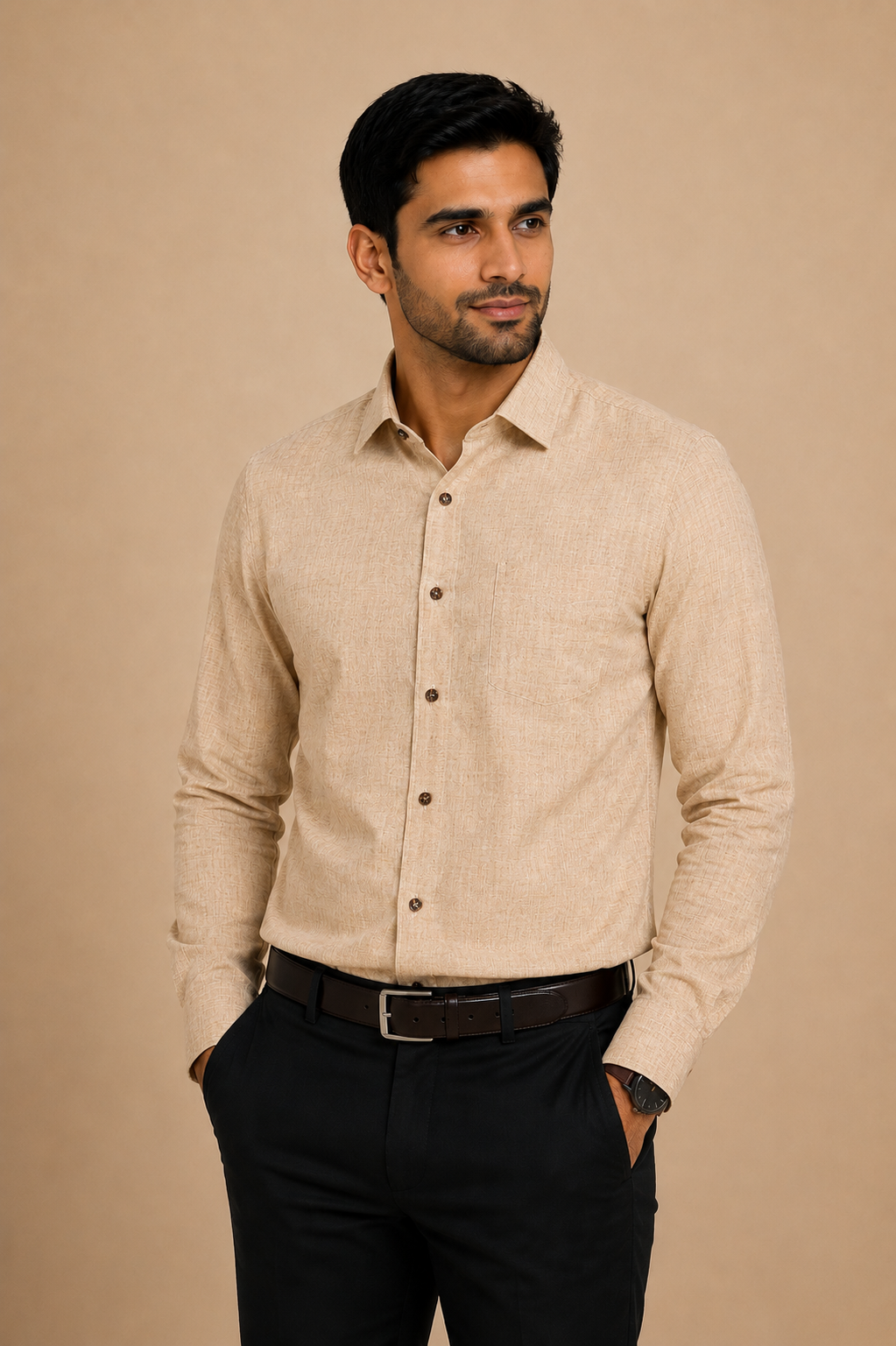 A man wearing a beige long-sleeve linen button-down shirt with black trousers and a brown belt, standing against a solid beige background.
