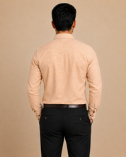 A man viewed from behind wearing a light peach-beige long-sleeve linen shirt and black trousers, standing against a solid beige background.