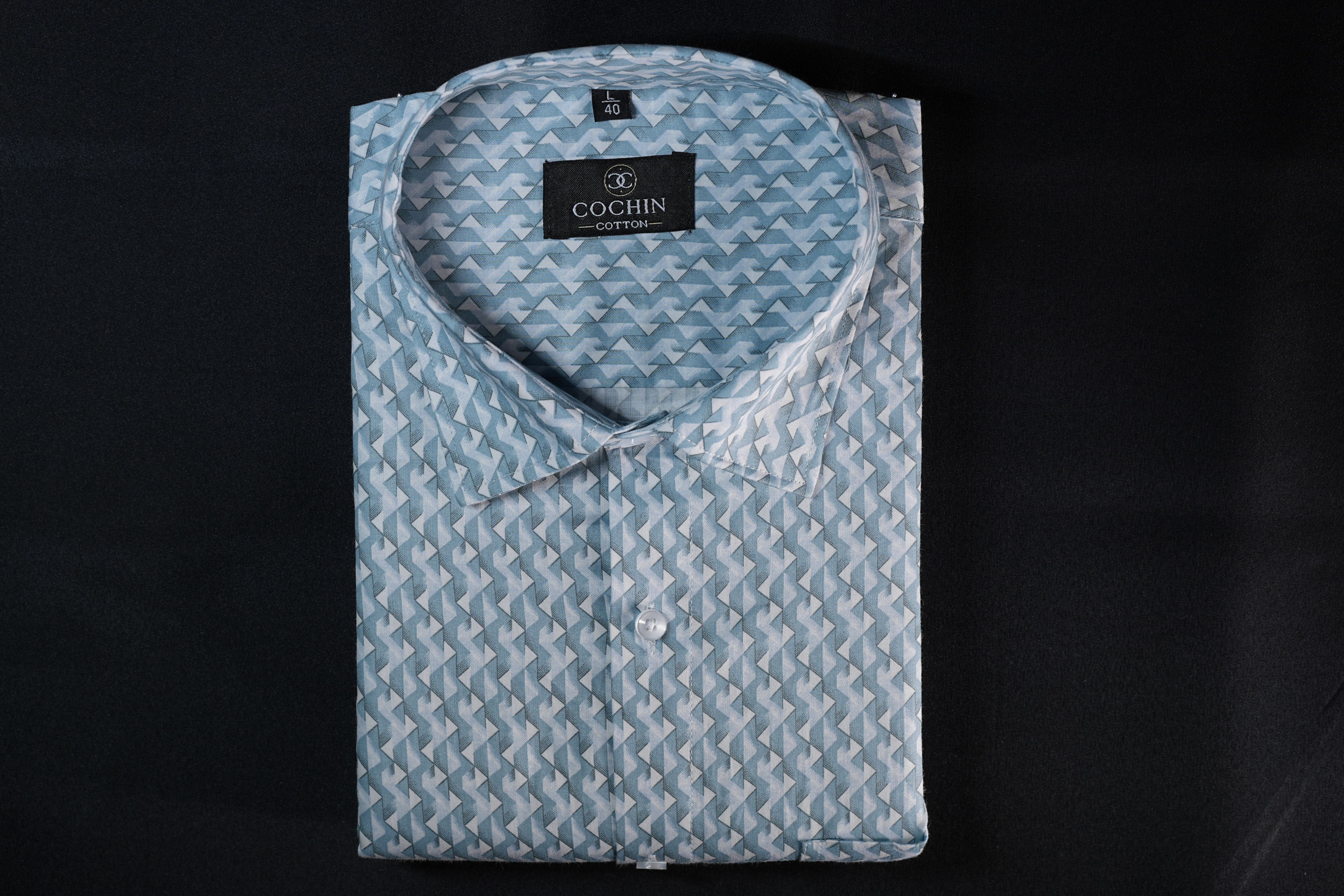 A folded light blue and white patterned dress shirt with a pointed collar and a visible Cochin label, laid flat against a black background.