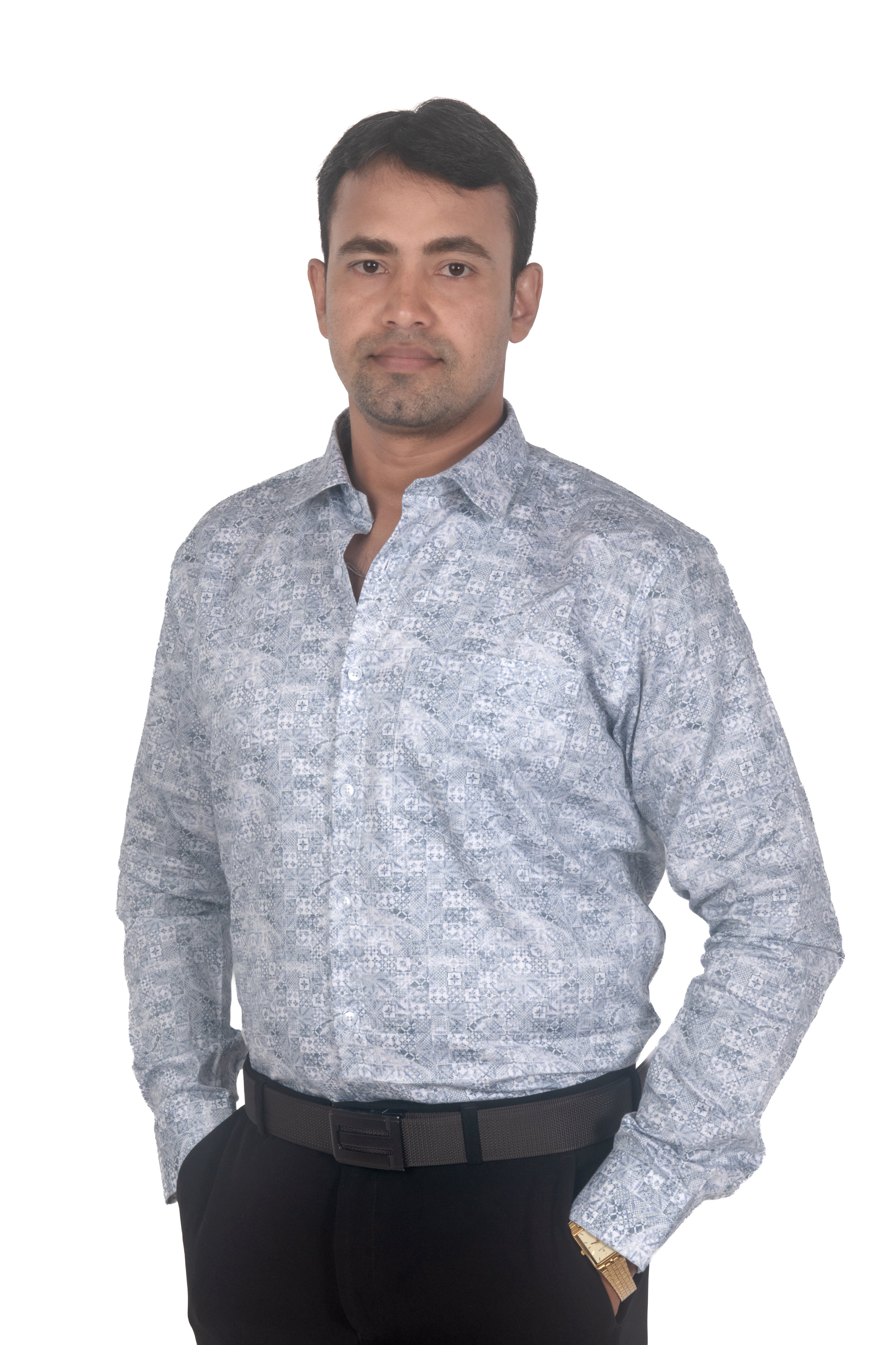 A man wearing a light blue and white patterned long-sleeve button-down shirt with black trousers, standing against a plain white background.