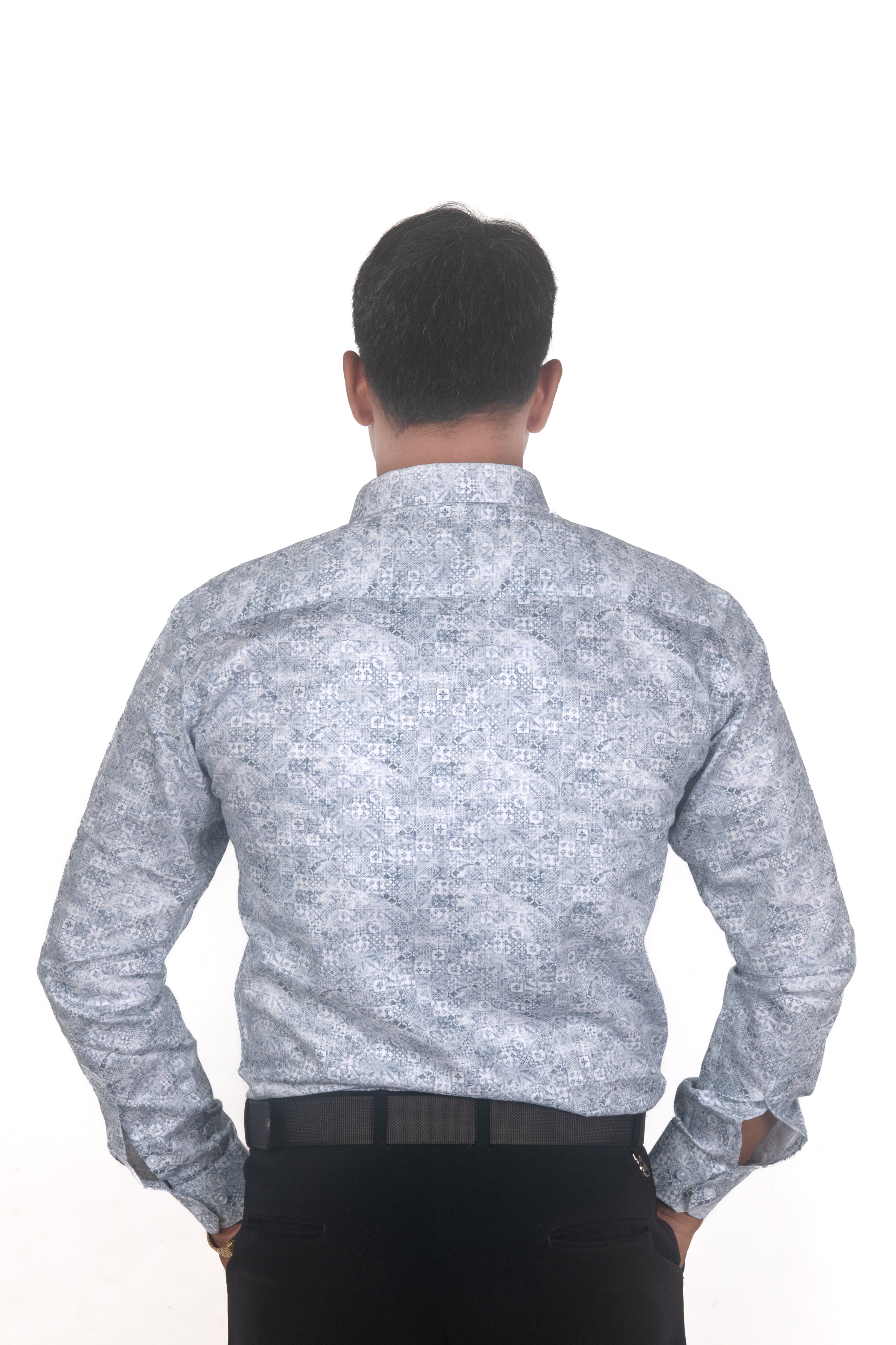 A man viewed from behind wearing a light blue and white patterned long-sleeve button-down shirt and black trousers, set against a plain white background.