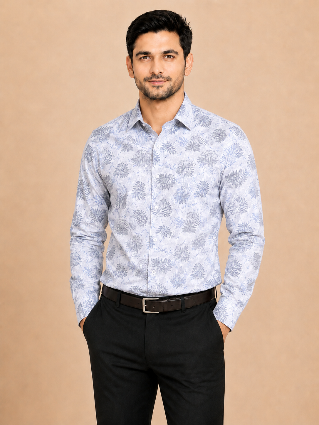 A man wearing a light blue and white patterned long-sleeve button-down shirt with black trousers, standing against a solid beige background.