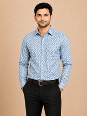 A man wearing a light blue and white patterned long-sleeve button-down shirt with black trousers, standing against a solid beige background.