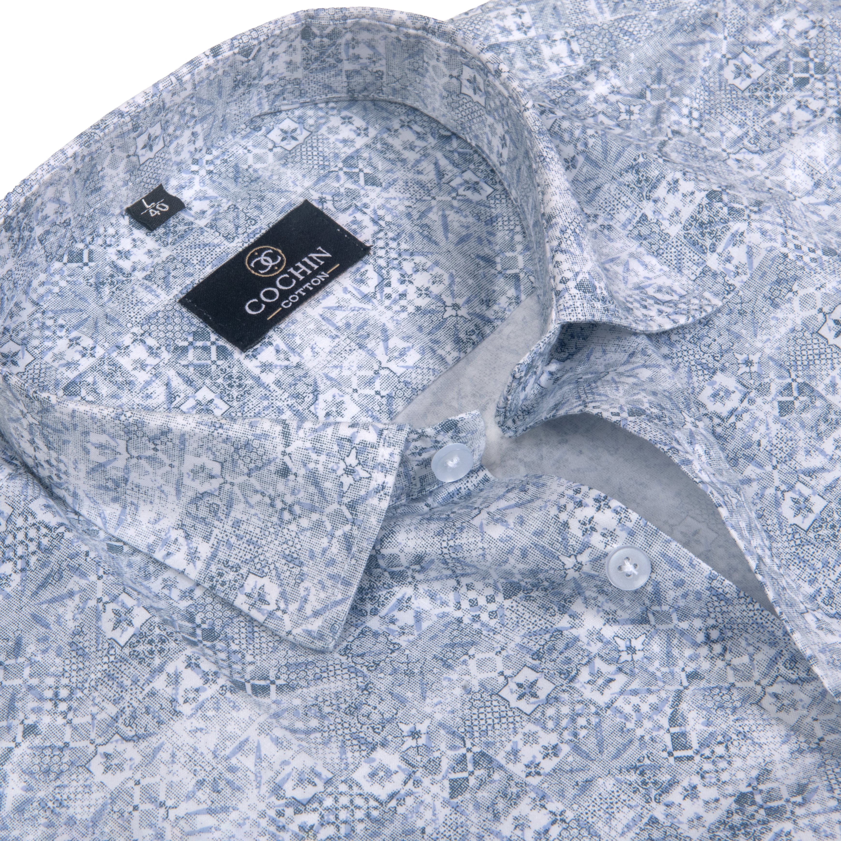 Close-up of a Cochin London dress shirt with a light blue and white geometric pattern, showing the collar, buttons, and inner brand label.