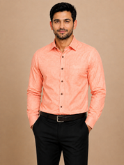 A man wearing a peach-colored long-sleeve linen shirt and black trousers, standing against a solid beige background.