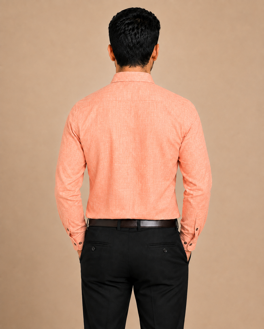 A man viewed from behind wearing a peach-colored long-sleeve textured shirt and black trousers, standing against a solid beige background.