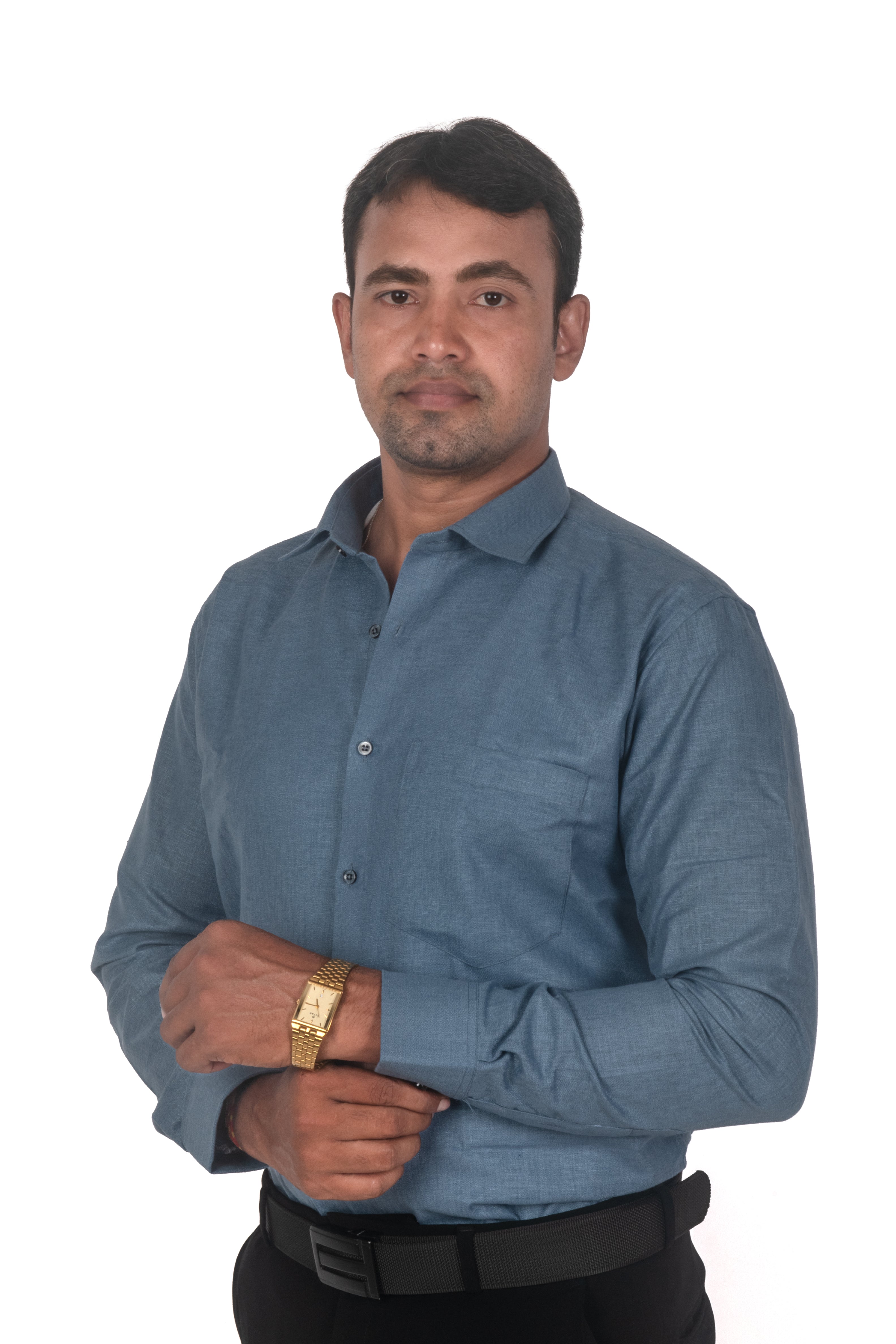 A man wearing a slate blue long-sleeve button-down shirt, black trousers, and a gold watch, standing against a plain white background.