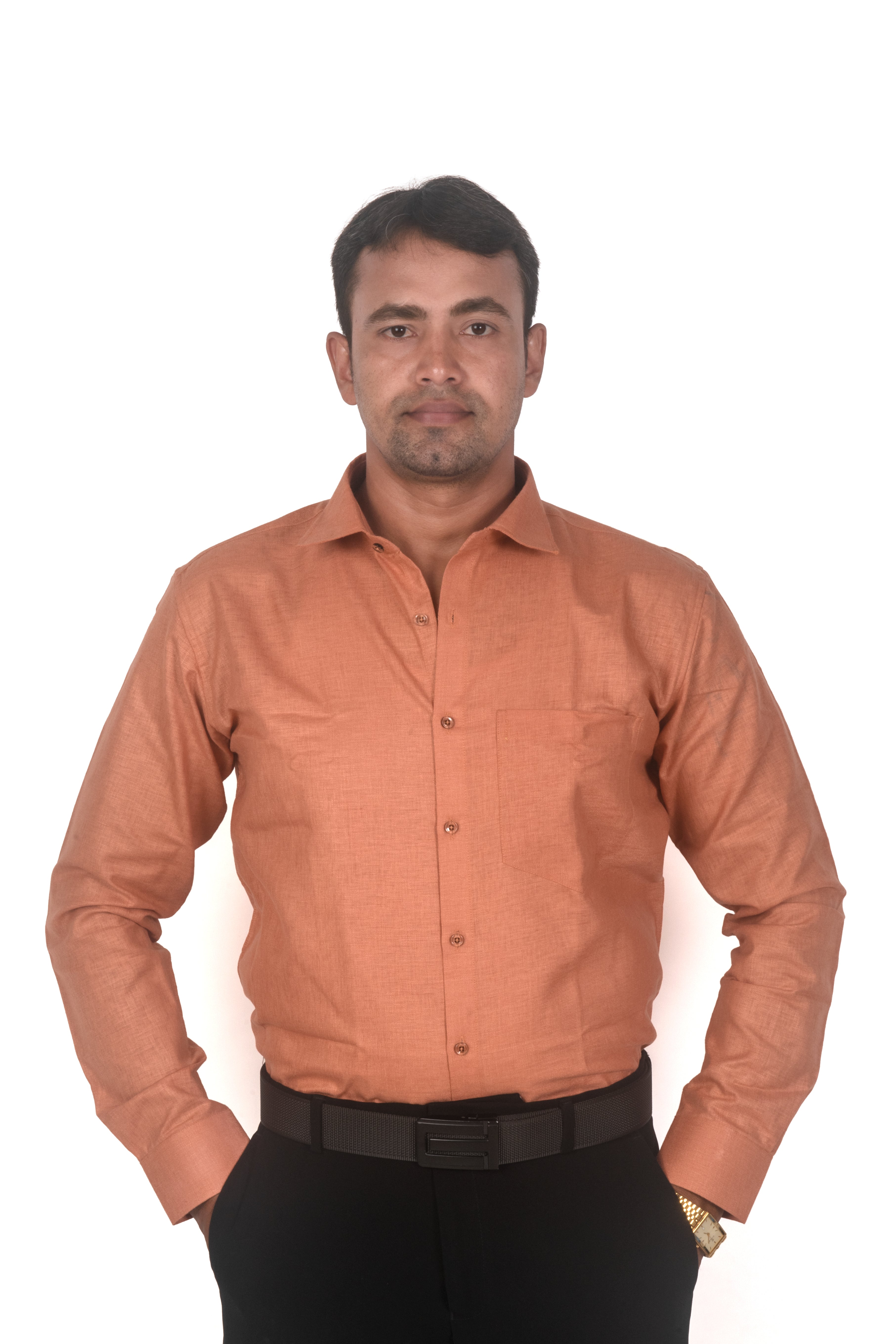 A man wearing a long-sleeve button-up shirt in a muted terracotta or burnt orange color, paired with black trousers and a black belt, standing against a plain white background.