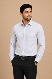A man wearing a light gray long-sleeve button-down dress shirt with a subtle micro-pattern, paired with black trousers and a dark brown belt, standing against a solid beige background.