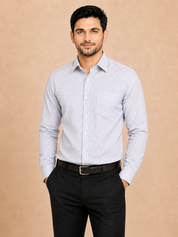 A man wearing a light gray long-sleeve button-down shirt with a subtle micro-pattern, paired with black trousers and a dark belt, standing against a solid beige background.