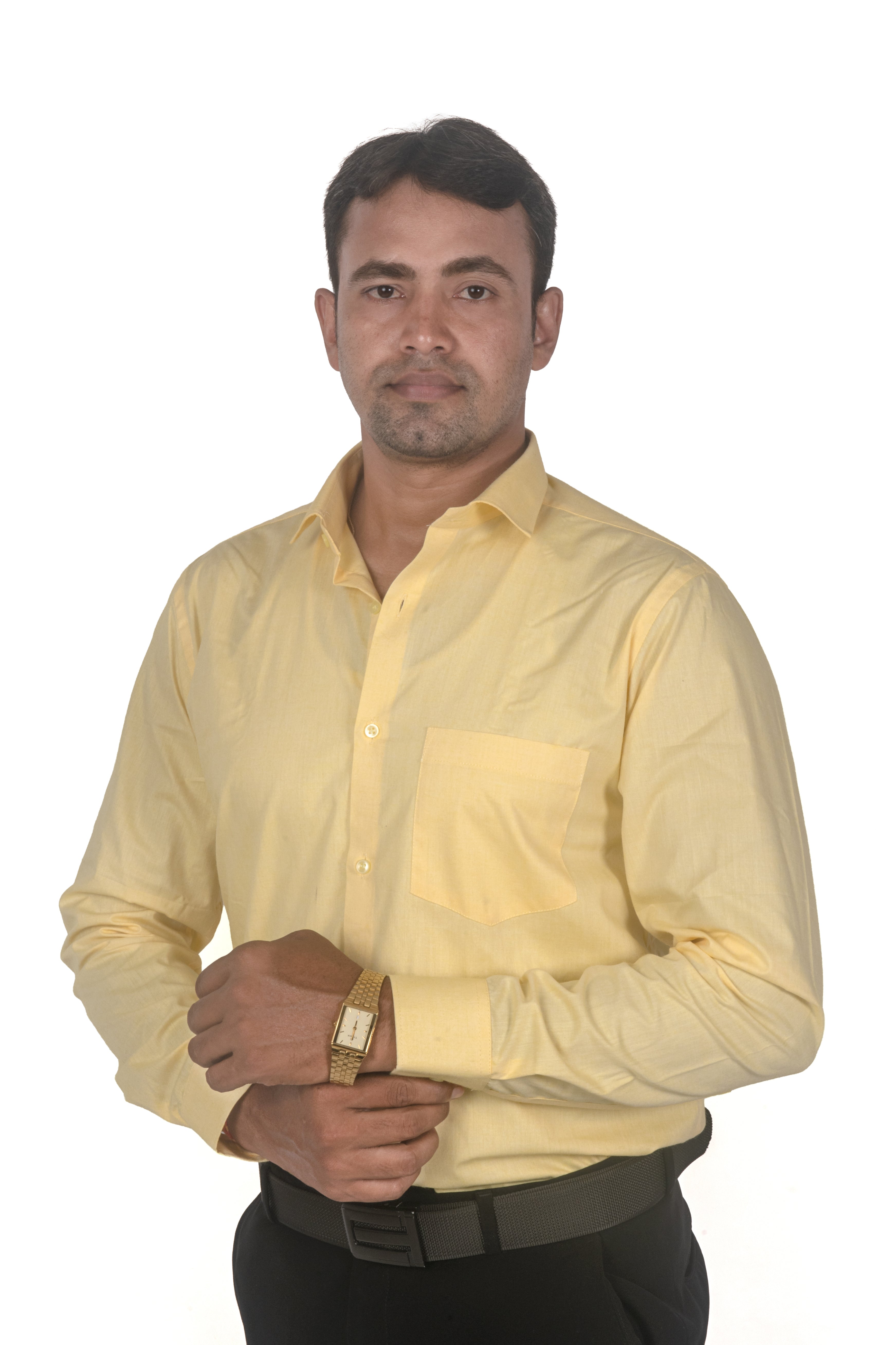 A man wearing a pale yellow long-sleeve button-up shirt and black trousers, standing against a plain white background.